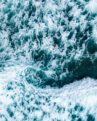 Aerial drone view of ocean surf crashing onto the shore. Turquoise water with white foam creates abstract natural patterns – a dynamic top-down shot of waves and sea textures.