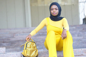 Elegant African woman in bright yellow outfit poses stylishly outdoors