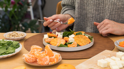 Woman eating healthy winter salad with citrus, persimmon and feta 