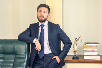 Professional man in formal suit poses beside desk with legal statue and books