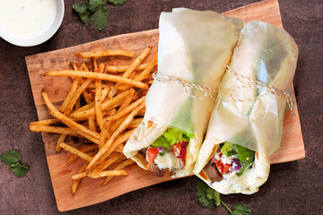 Greek gyros pita wraps with fries and tzatziki. Top view serving board on a dark background.