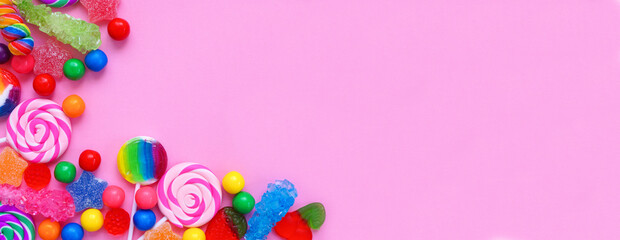 Colorful collection of candies. Above view corner border over a pink banner background.