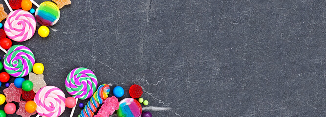 Sweet collection of candies. Overhead view corner border over a black stone banner background.