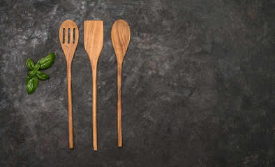 Wooden cutlery on black textured background with basil leaf and copy-space.