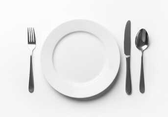 Top down studio shot of white plate with fork knife and spoon ceramic