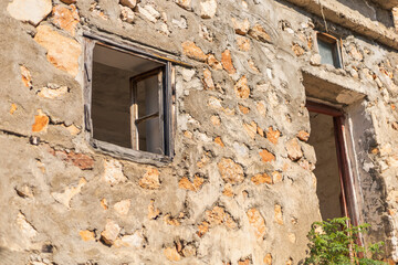 Sunlight highlights an abandoned building's weathered stone wall adorned with two window openings....