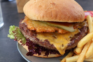 Close-up of a cheeseburger with inventive toppings on a plate, served alongside golden French fries, all placed on a tabletop. Perfect for food-related content and mouth-watering promotional use.