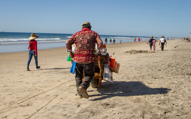 A vendor pushing a cart of food items along a beach