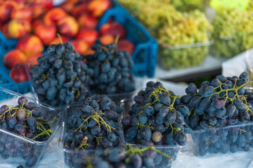 Clusters of freshly picked black grapes sit in clear containers alongside vibrant red apples at a...