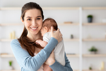 Fototapeta premium Happy Maternity Time. Portrait Of Beautiful Young Mother Embracing Adorable Newborn Child And Smiling At Camera, Happy Millennial Woman Bonding With Her Little Infant Baby At Home, Copy Space