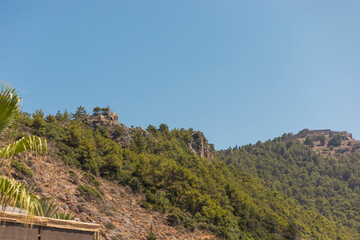 A breathtaking view of rolling hills adorned with dense forests under a brilliant blue sky. The...