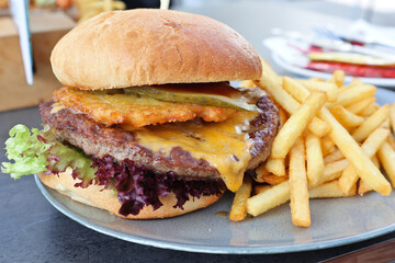 Tasty cheeseburger with lettuce and cheese, served with crispy fries on a plate at an outdoor café. A savory comfort food meal perfect for lunch or dinner.