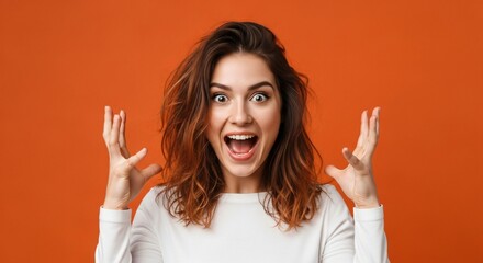 Young woman expresses extreme joy and excitement with wide eyes and open mouth against a vibrant orange background