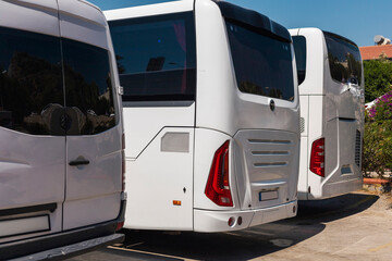 Several white buses are parked closely together at a transportation hub under clear blue skies. The...