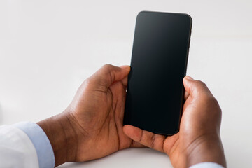 Online doctor and remote advice. Black man doctor using smartphone with blank screen, consulting...