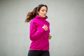 Focused woman jogging in pink windbreaker against gray wall © Paula