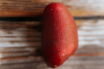 A single red potato lies on a rustic wooden surface, highlighting its textured skin and vibrant...