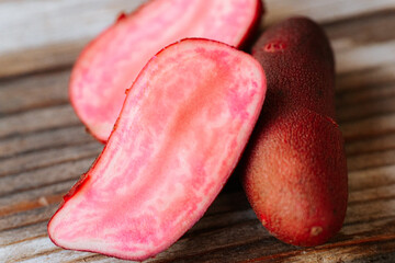 A detailed macro shot of a pink-fleshed potato cut open on a rustic wooden surface. The vibrant colors and texture stand out. Contains text.