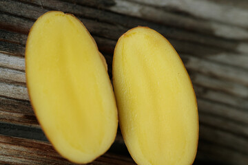 A yellow potato, cut in half, revealing its smooth interior, and placed on a worn wooden background.