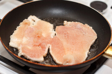 Slices of meat chicken brisket cooking in a frying pan. Meat is light pink arranged evenly in pan