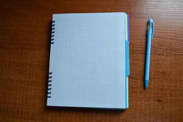 a stack of squared notebooks with a blue pen lying on a wooden desk, top notebook is spiral-bound...