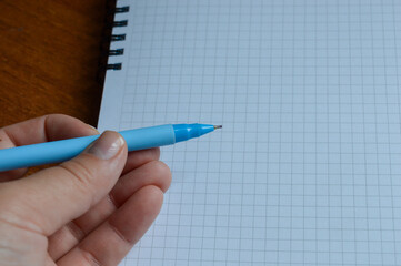 a stack of squared notebooks with a blue pen lying on a wooden desk, top notebook is spiral-bound...