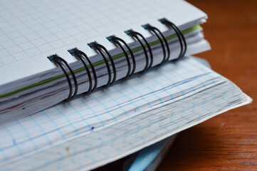 a stack of squared notebooks with a blue pen lying on a wooden desk, top notebook is spiral-bound...
