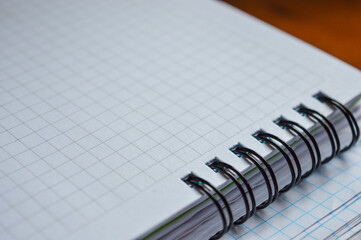 a stack of squared notebooks with a blue pen lying on a wooden desk, top notebook is spiral-bound...