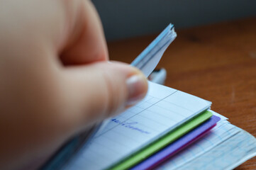 close-up of a hand flipping through pages of a squared notebook with colorful covers, on a wooden...