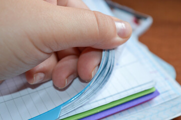 close-up of a hand flipping through pages of a squared notebook with colorful covers, on a wooden...