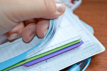close-up of a hand flipping through pages of a squared notebook with colorful covers, on a wooden...