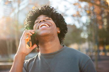 Man laughing hard during phone call in sunlit park