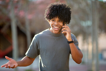 Smiling young Cuban man talking on smartphone outdoors in casual outfit