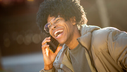 Laughing young mixed race man in winter coat talking on smartphone
