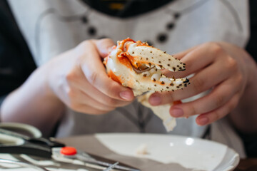 Person cracking a crab claw by hand at a seafood restaurant, with utensils and plate visible. 