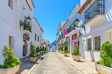 Altea old town narrow street Carrer Sant Miquel, typical white houses traditional buildings and green bushes in sunny summer day, Altea city historical centre Casco Antiguo, Alicante province, Spain