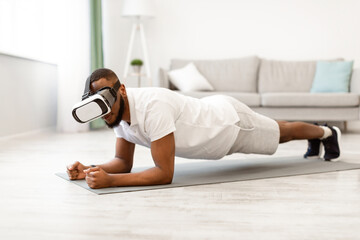 Naklejka premium VR Workout. Black Sporty Man Wearing Virtual Reality Glasses Standing In Plank Exercising During Training In Digital Gym At Home. Augmented Reality Application For Smart Fitness