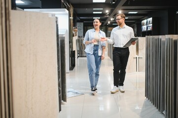 Shop assistant showing ceramic tiles to customer in store