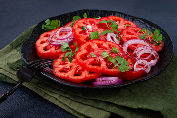 Freshly sliced tomatoes and red onions, garnished with herbs, on a black plate, summer salad, no people