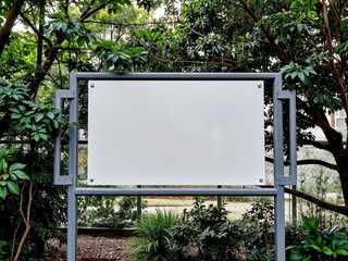 Empty white billboard surrounded by greenery in a park setting with room for text