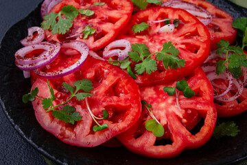 Freshly sliced tomatoes and red onions, garnished with herbs, on a black plate, summer salad, no people