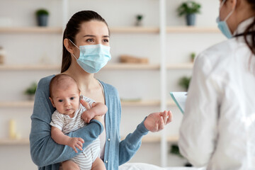 Unrecognizable doctor in protective medical mask visiting mother with newborn baby at home,...