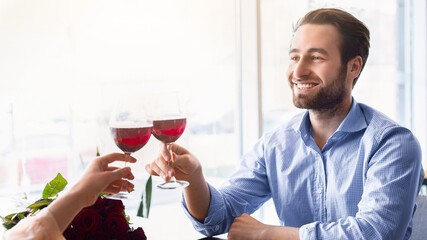 Affectionate millennial couple celebrating anniversary together, drinking wine, making toast at cozy cafe. Lovely woman and her young husband enjoying romantic dinner on Valentine's Day