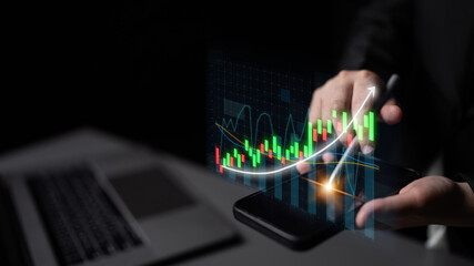A businessman analyzes a digital financial chart displayed on a smartphone, illustrating stock market trends. The dark office background highlights the modern technology focus. Impute