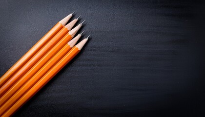 four vibrant orange pencils arranged on a black chalkboard surface ideal for educational materials