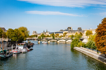 Stunning autumnal cityscape along the Seine, featuring bridges, riverboats, and the magnificent Louvre