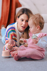 Vertical portrait shows a girl in pink overalls on a grey rug, stacking pastel cups with curiosity...