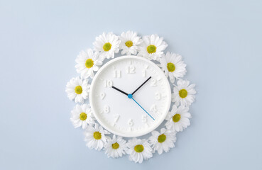 Wall clock decorated with chamomile flowers on a blue background. Concept of a new day or...