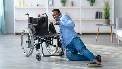 Young black man with disability lying on floor after falling down from wheelchair at home. Helpless...