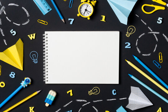 Creative school background with empty notebook surrounded by yellow and blue stationery on a blackboard. Concept of back to school or learning. - Powered by Adobe